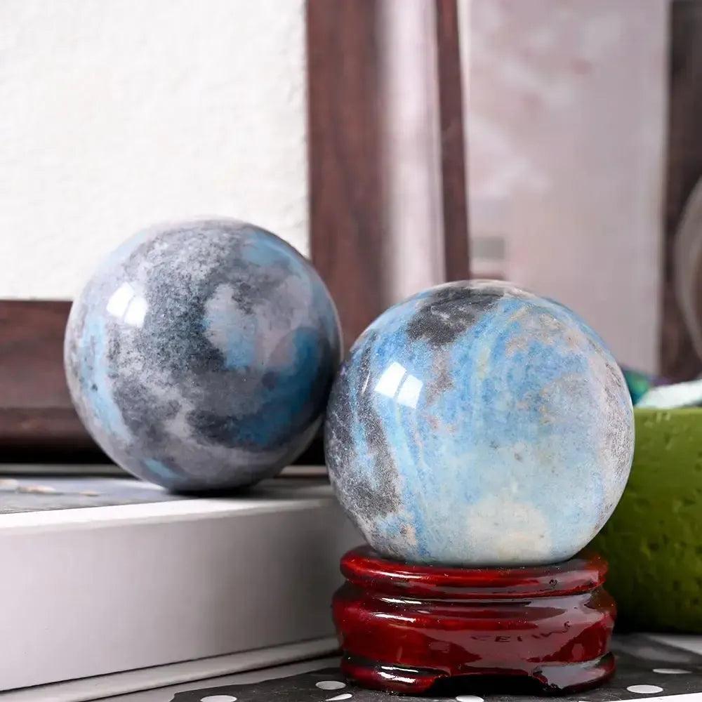 Polished Blue Trolleite sphere from Crystal Destiny, showcasing blue-gray hues and natural inclusions on a wooden stand.