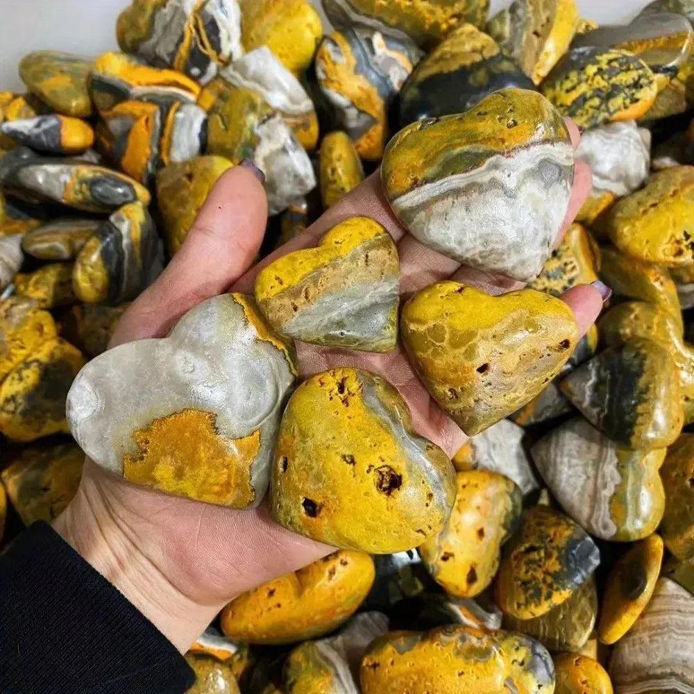 Hand holding polished Bumble Bee Jasper crystal hearts, vibrant yellow, orange, and black, from Crystal Destiny.