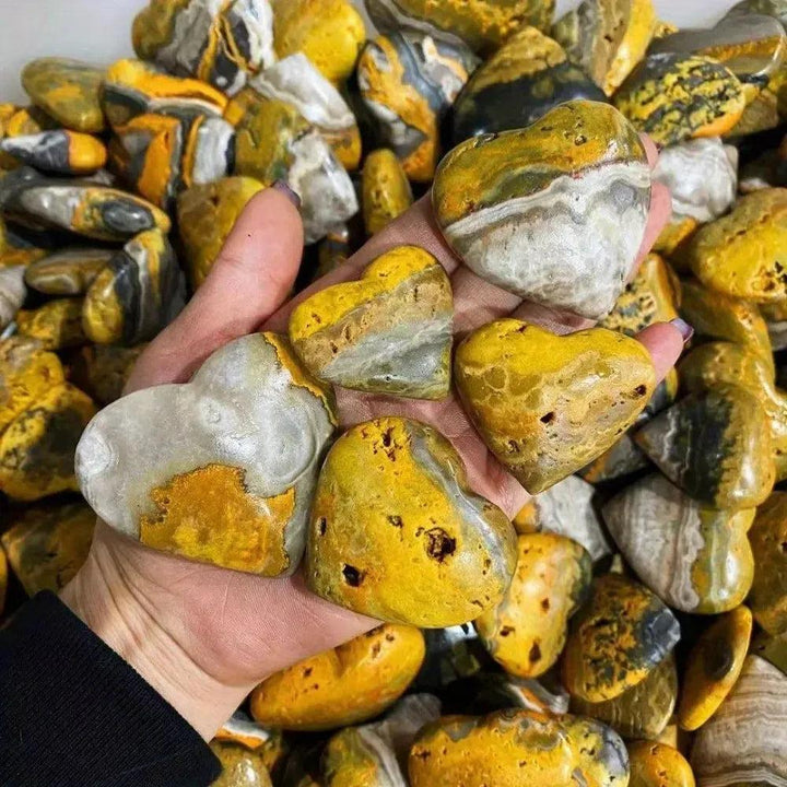 Hand holding polished Bumble Bee Jasper crystal hearts, vibrant yellow, orange, and black, from Crystal Destiny.