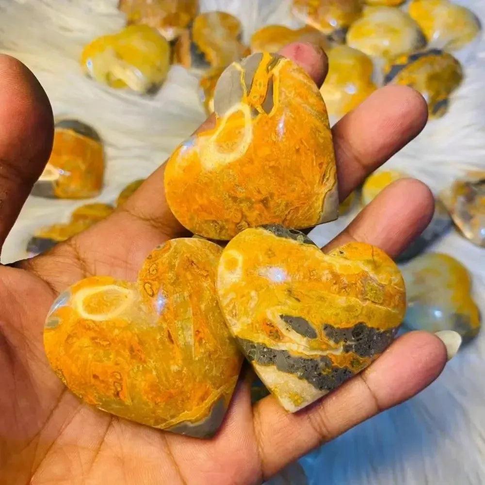 Crystal Destiny's Bumble Bee Jasper heart crystals, vibrant yellow, orange, and black, held in a hand.