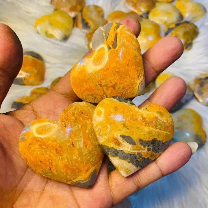 Crystal Destiny's Bumble Bee Jasper heart crystals, vibrant yellow, orange, and black, held in a hand.