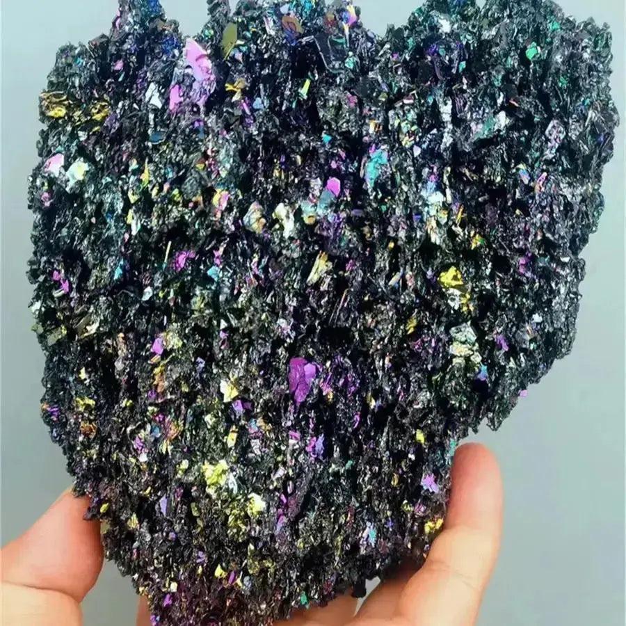 Hand holding a raw Carborundum Silicon Carbide crystal with intense iridescent rainbow surface coloration.