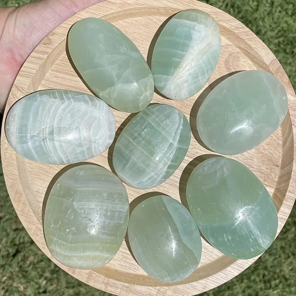 Polished Caribbean Calcite palm stones in calming ocean blue and white on a wooden tray.