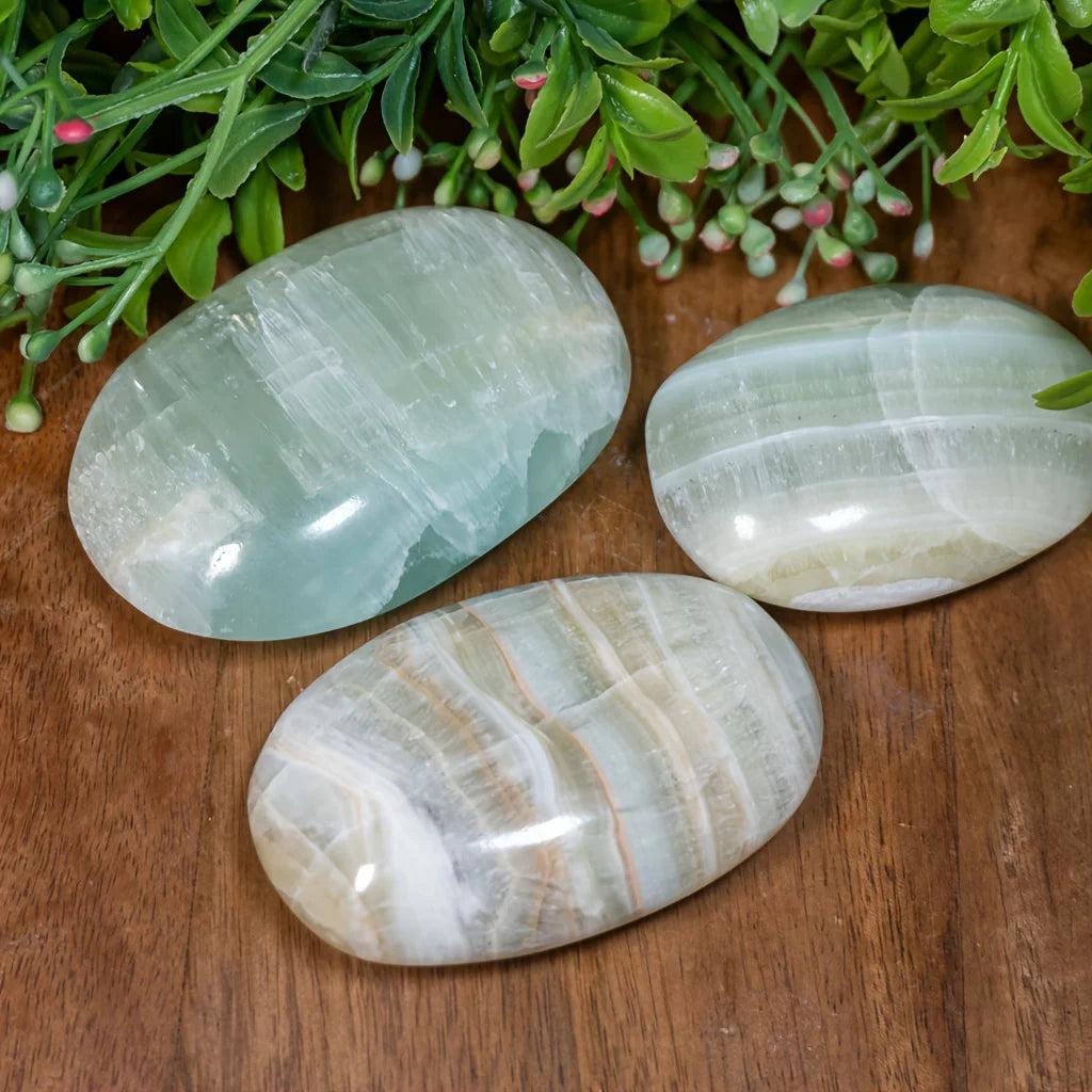 Polished Caribbean Calcite palm stones in soothing ocean blue and tan, perfect for calming anxiety.