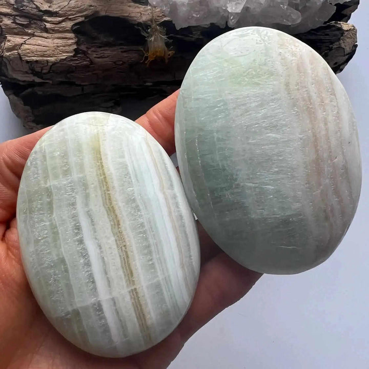 Two smooth, hand-polished Caribbean Calcite palm stones featuring calming ocean blue, white, and soft brown swirls.