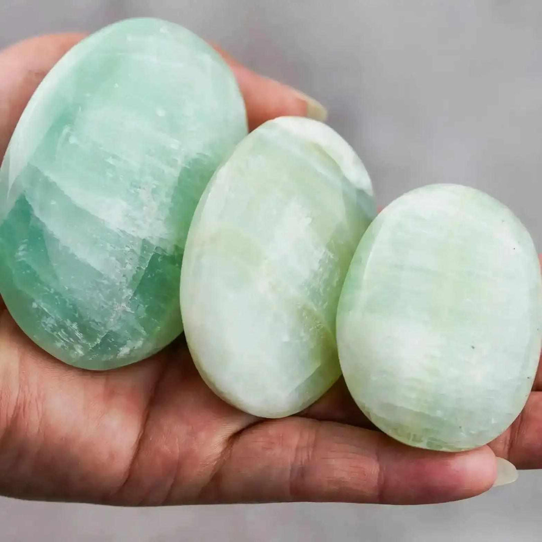 Three smooth, ocean-blue Caribbean Calcite palm stones held in a hand, perfect for meditation and calming energy.