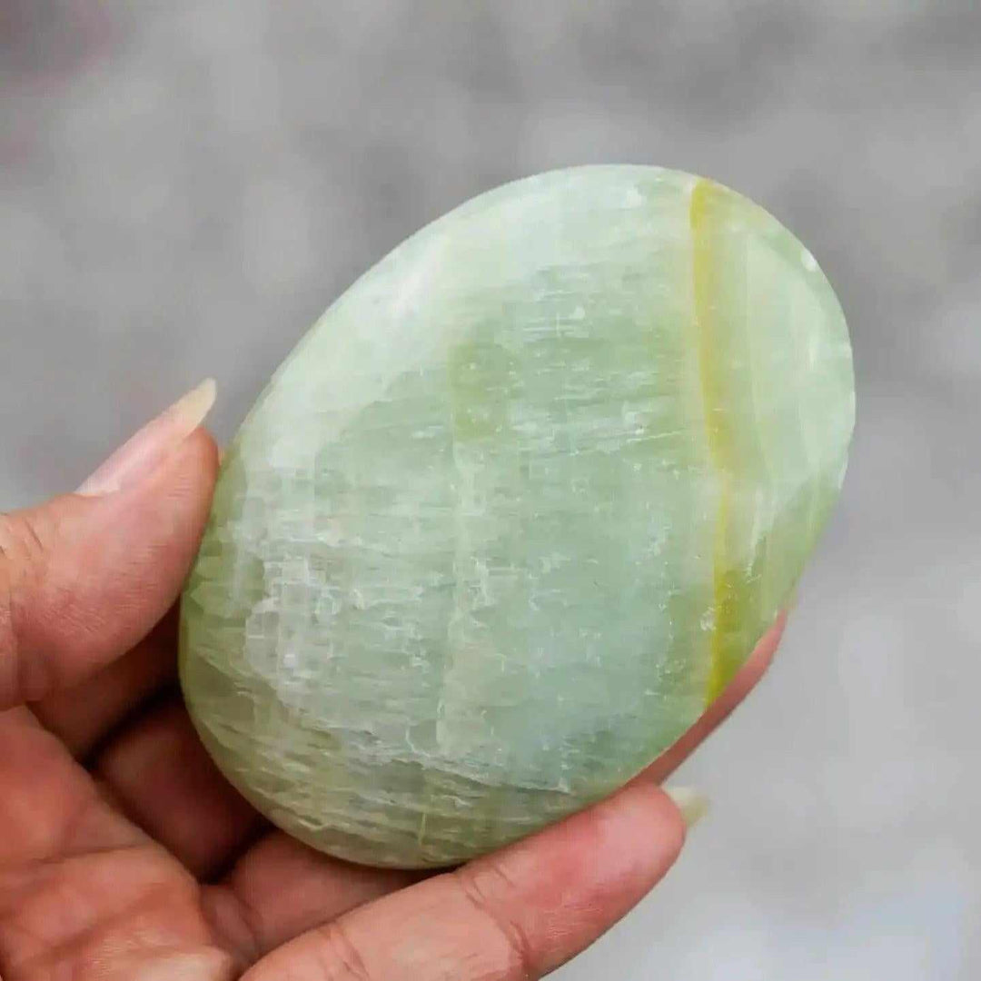 Smooth, hand-polished Caribbean Calcite palm stone featuring calming ocean-blue and white swirls for meditation.