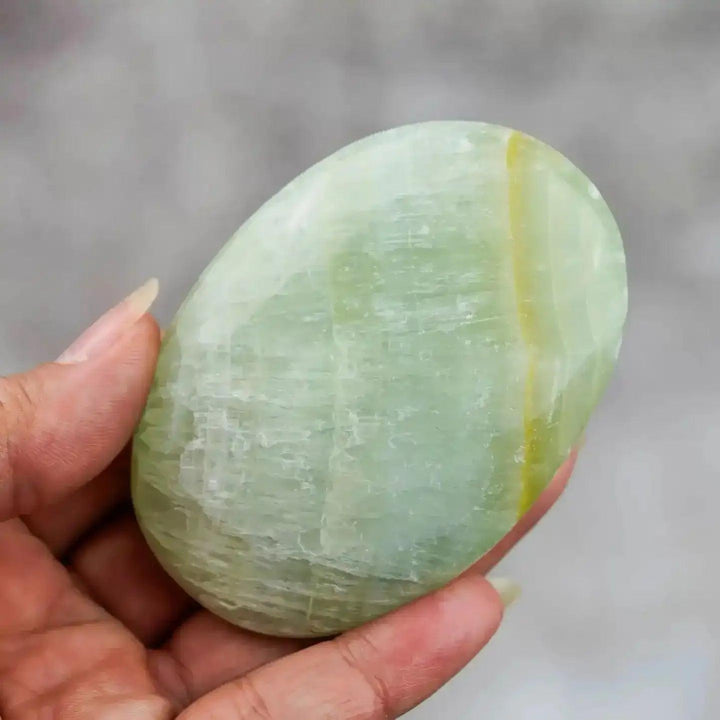 Smooth, hand-polished Caribbean Calcite palm stone featuring calming ocean-blue and white swirls for meditation.