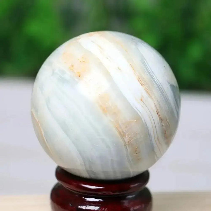 Crystal Destiny Caribbean Calcite sphere with soft blue, white, and tan bands, on a dark wood stand.