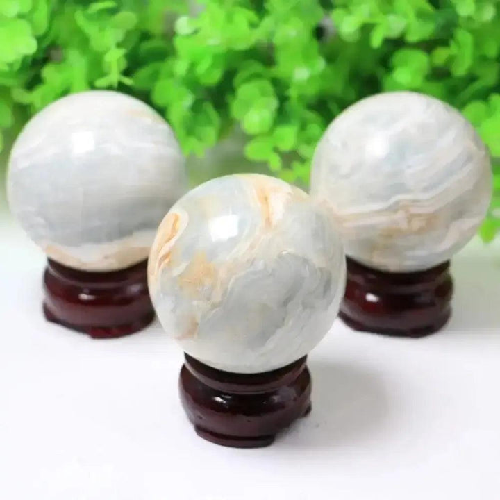 Three polished Caribbean Calcite spheres from Crystal Destiny, featuring soothing blue, white, and tan bands on dark wood stands.
