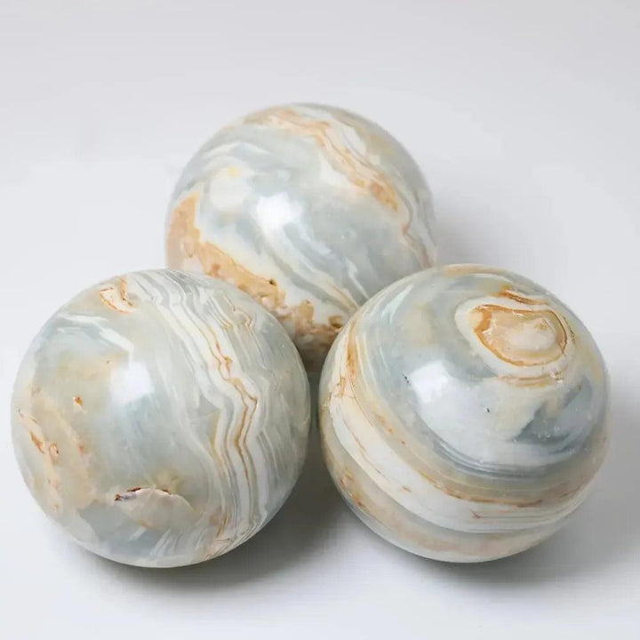 Three polished Caribbean Calcite spheres from Crystal Destiny, featuring soft blue, white, and tan swirling patterns.
