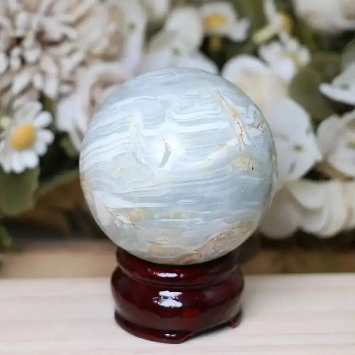Caribbean Calcite sphere from Crystal Destiny, featuring soft blue and white bands on a dark wood stand.