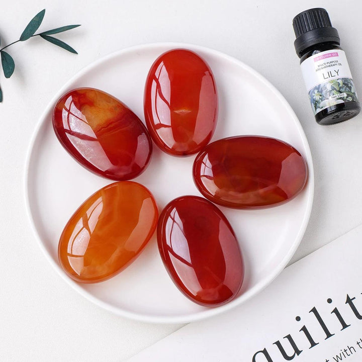 Polished orange-red Carnelian crystal palm stones for grounding, courage, and creativity in a smooth, handheld design.
