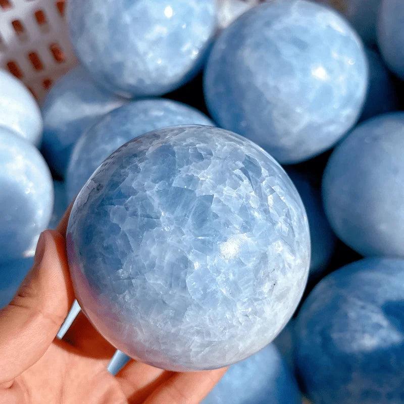 Hand holding a polished Celestite Crystal Sphere, showcasing its soft, powdery blue hue for deep calm and clarity.