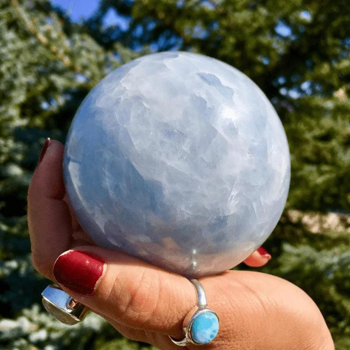 Celestite Crystal Polished Sphere, a soft blue natural stone ball held in a hand, promoting calm and clarity.