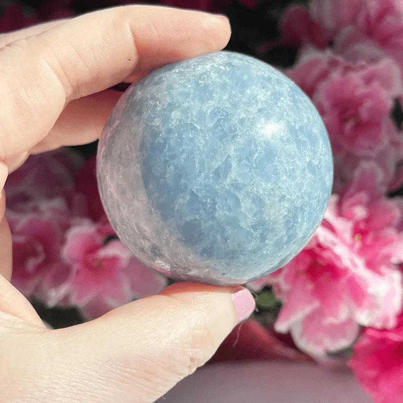 Hand holding a polished Celestite Crystal Sphere, a soft blue natural stone ball for peace and tranquility.