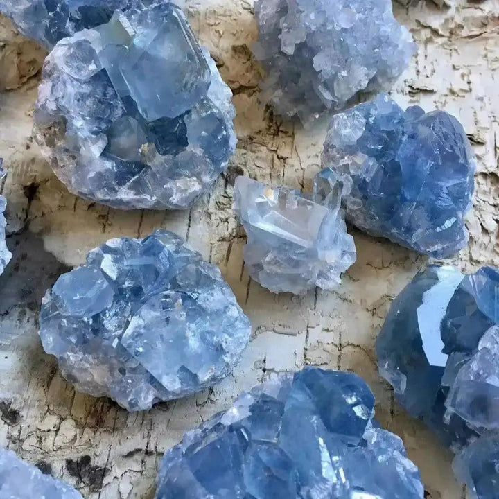 Raw Celestite clusters for Peace & Tranquility, featuring soft blue crystals on a natural wood background.