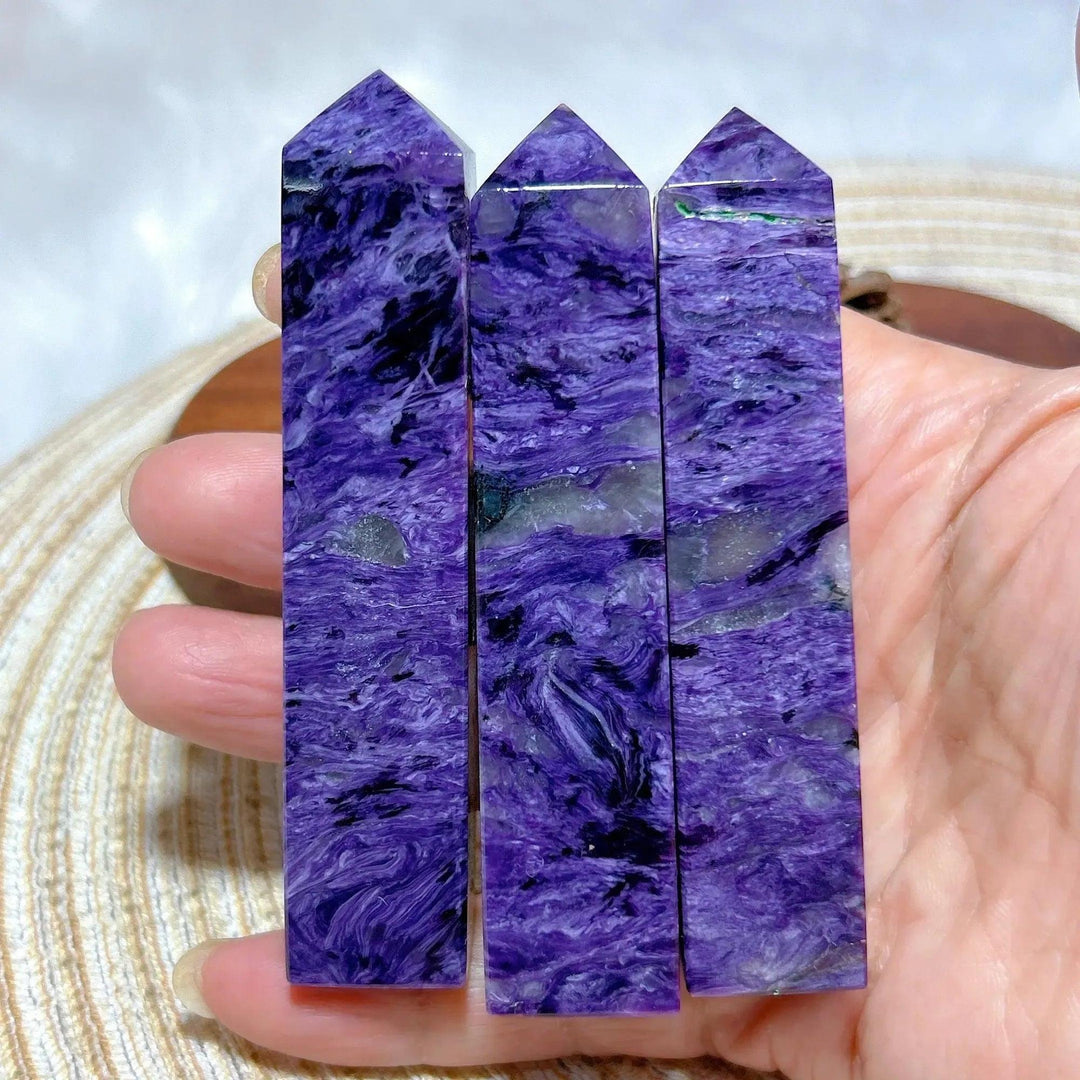 Three Charoite point towers, rich swirling violet, lavender, and white, held in a hand. Crystal Destiny.