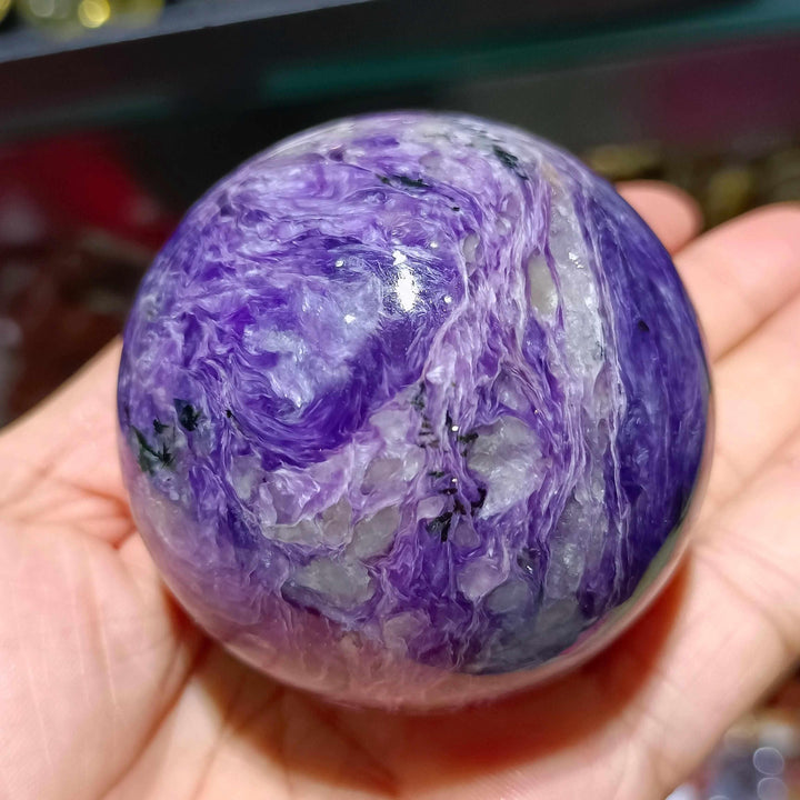 Polished Charoite sphere featuring swirling violet, lavender, and white patterns for spiritual transformation and protection.