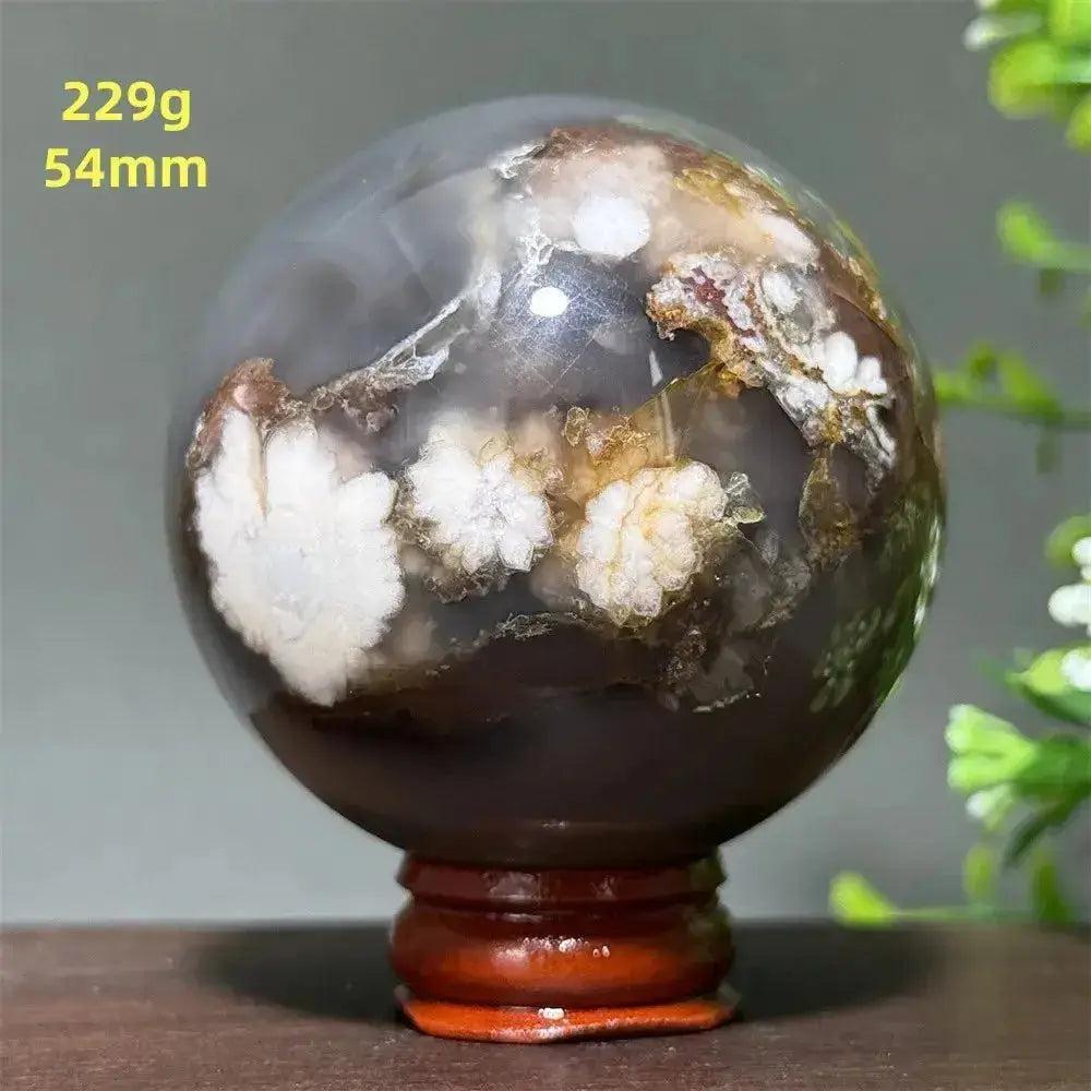 Cherry Agate Crystal Sphere: Polished red, pink, and gray orb with unique banding on a wooden stand.