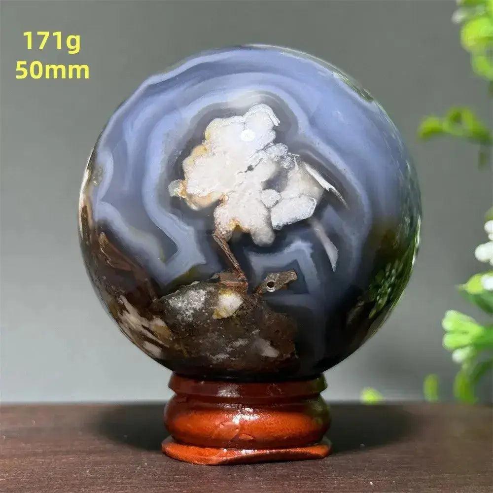 Polished gray and white agate crystal sphere with a unique tree-like inclusion, on a wooden stand.