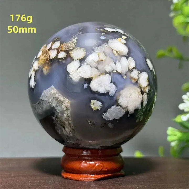 Polished gray agate crystal sphere with white and gold floral inclusions on a wooden stand.