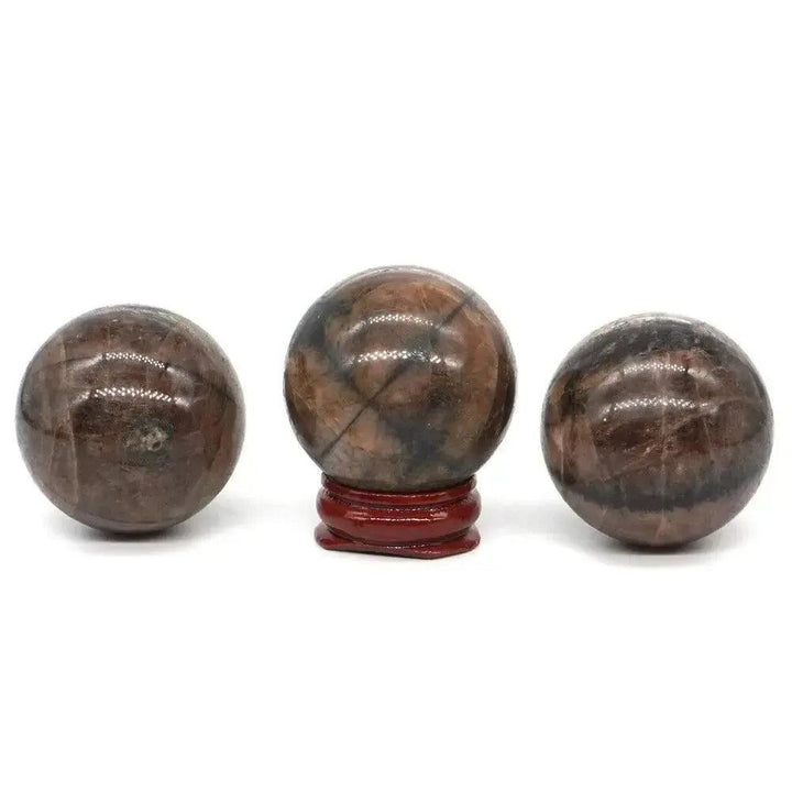 Three polished brown Chiastolite spheres, one on a red stand, showcasing unique dark cross patterns for protection and grounding.
