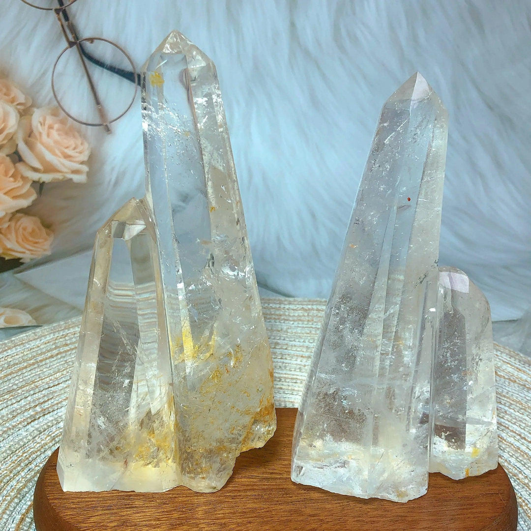 Two clear quartz crystal double mountain towers with natural, unpolished peaks on a wooden base.