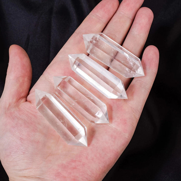 Four clear quartz double terminated points, 40-80mm, held in a hand, amplifying healing and clarity.