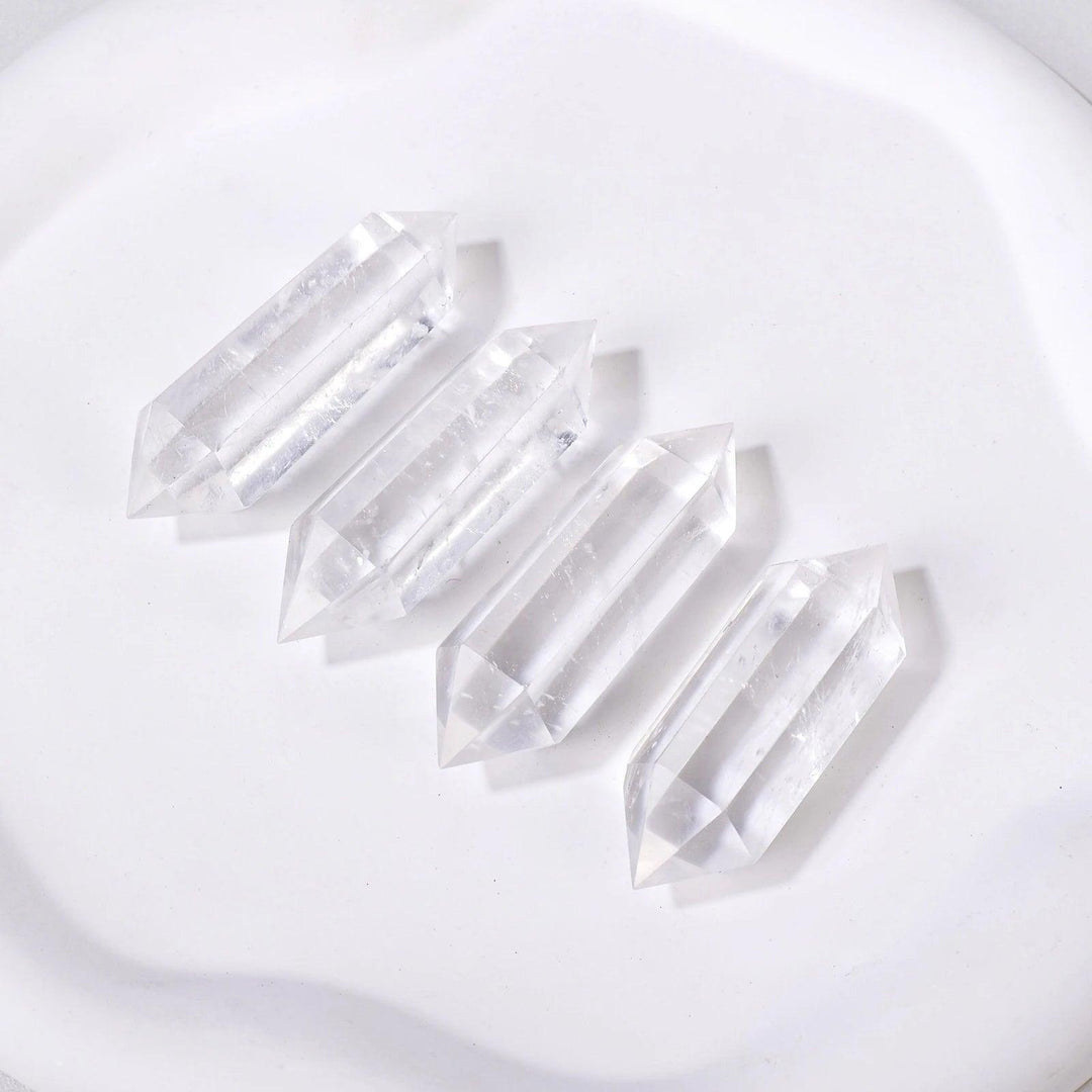 Four clear quartz crystal double terminated points, radiating clarity and amplification, on a white surface.