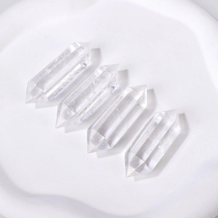 Four clear quartz crystal double terminated points, radiating clarity and amplification, on a white surface.