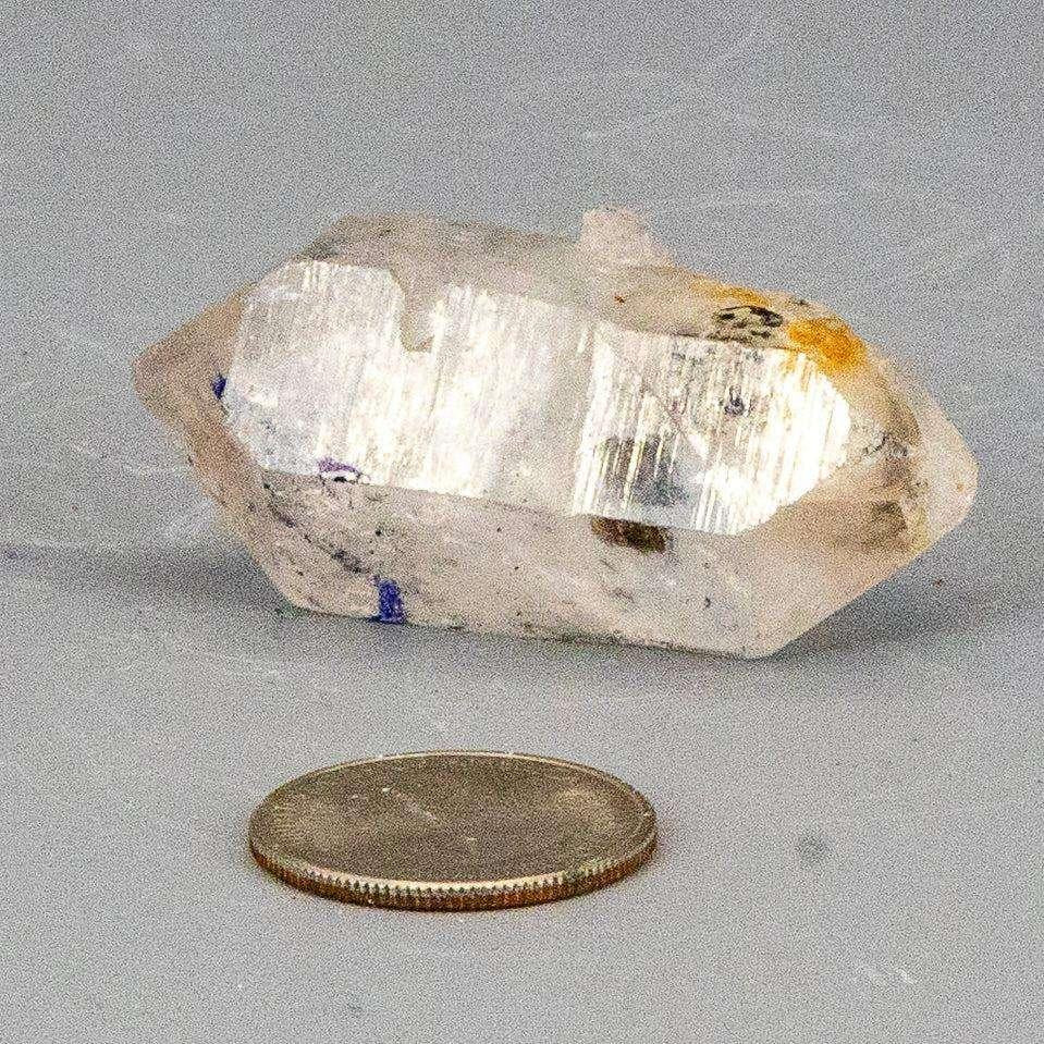 Clear, natural Double Terminated Quartz Point, 2 inches long, with subtle blue and orange inclusions, next to a quarter.