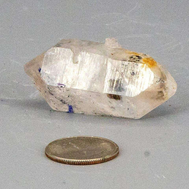 Clear, natural Double Terminated Quartz Point, 2 inches long, with subtle blue and orange inclusions, next to a quarter.