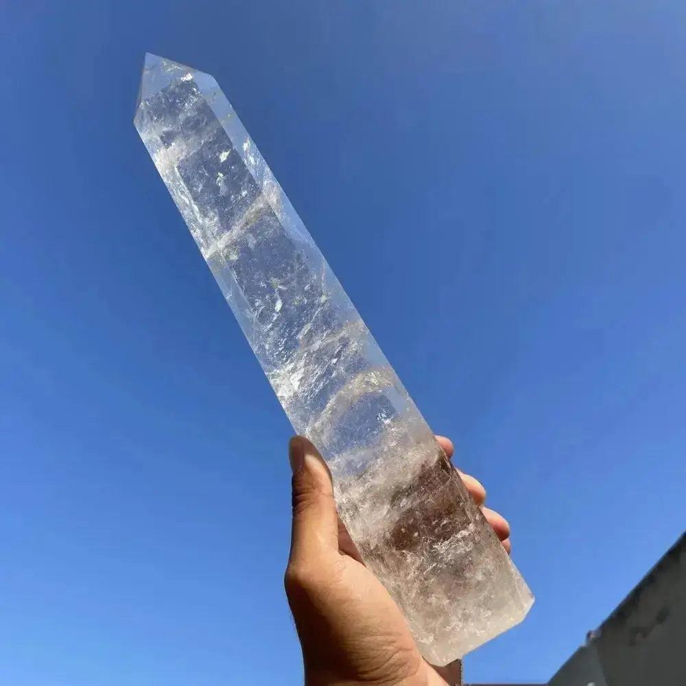 Clear Quartz Hexagonal Crystal Tower, a polished natural crystal obelisk, held against a bright blue sky.