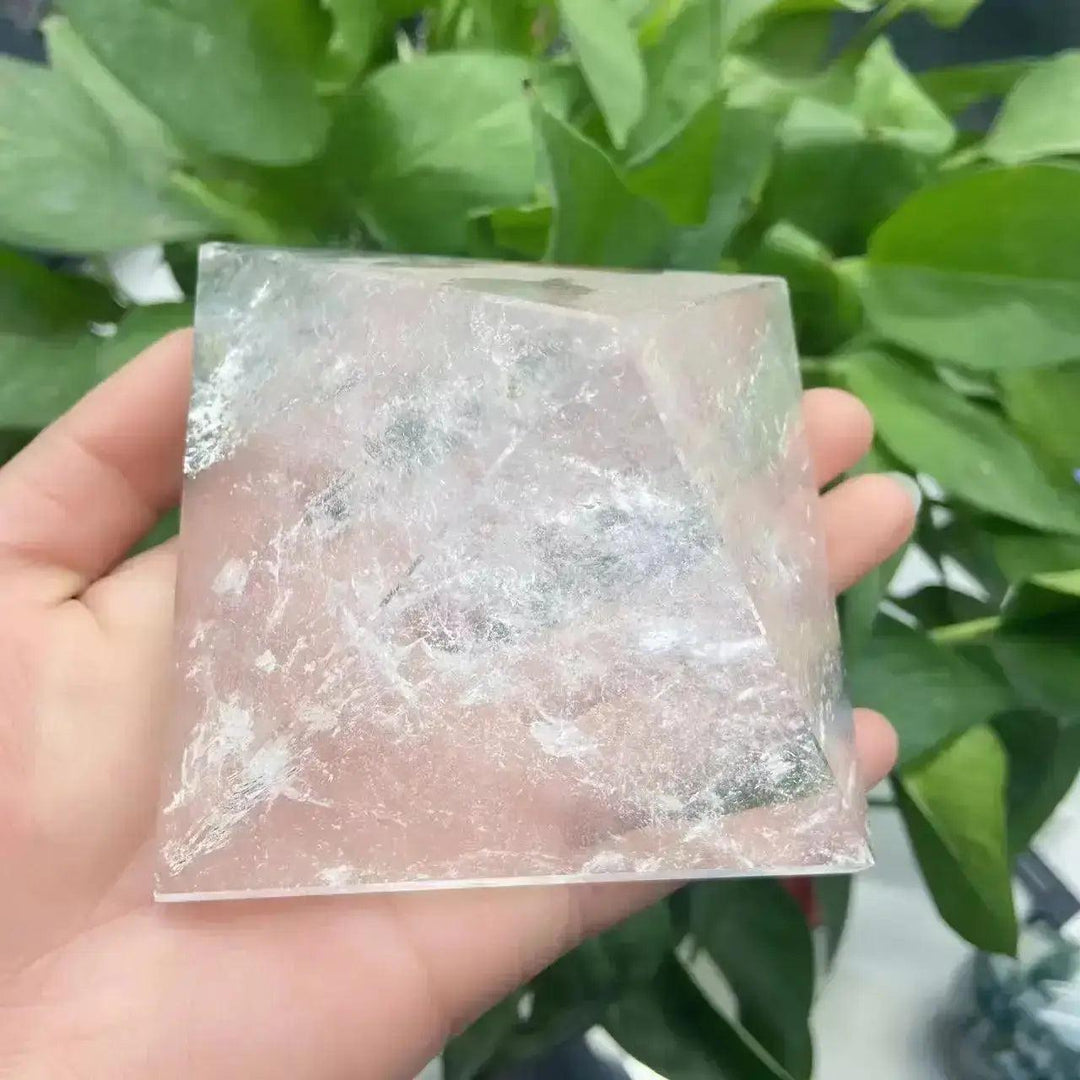 Clear Quartz Crystal Pyramid, a natural amplifier stone, held in hand against green foliage.