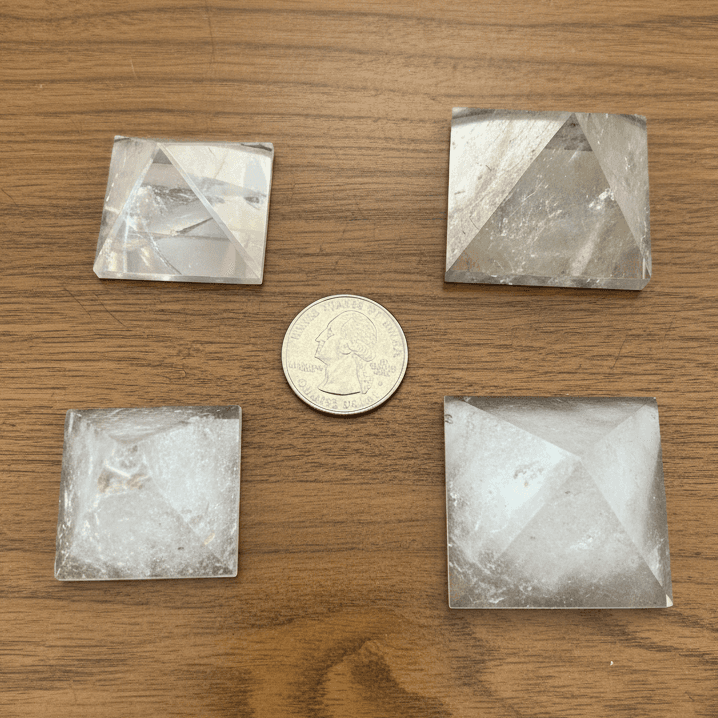 Four clear quartz crystal pyramids, naturally transparent with unique internal clarity, on a wood surface.