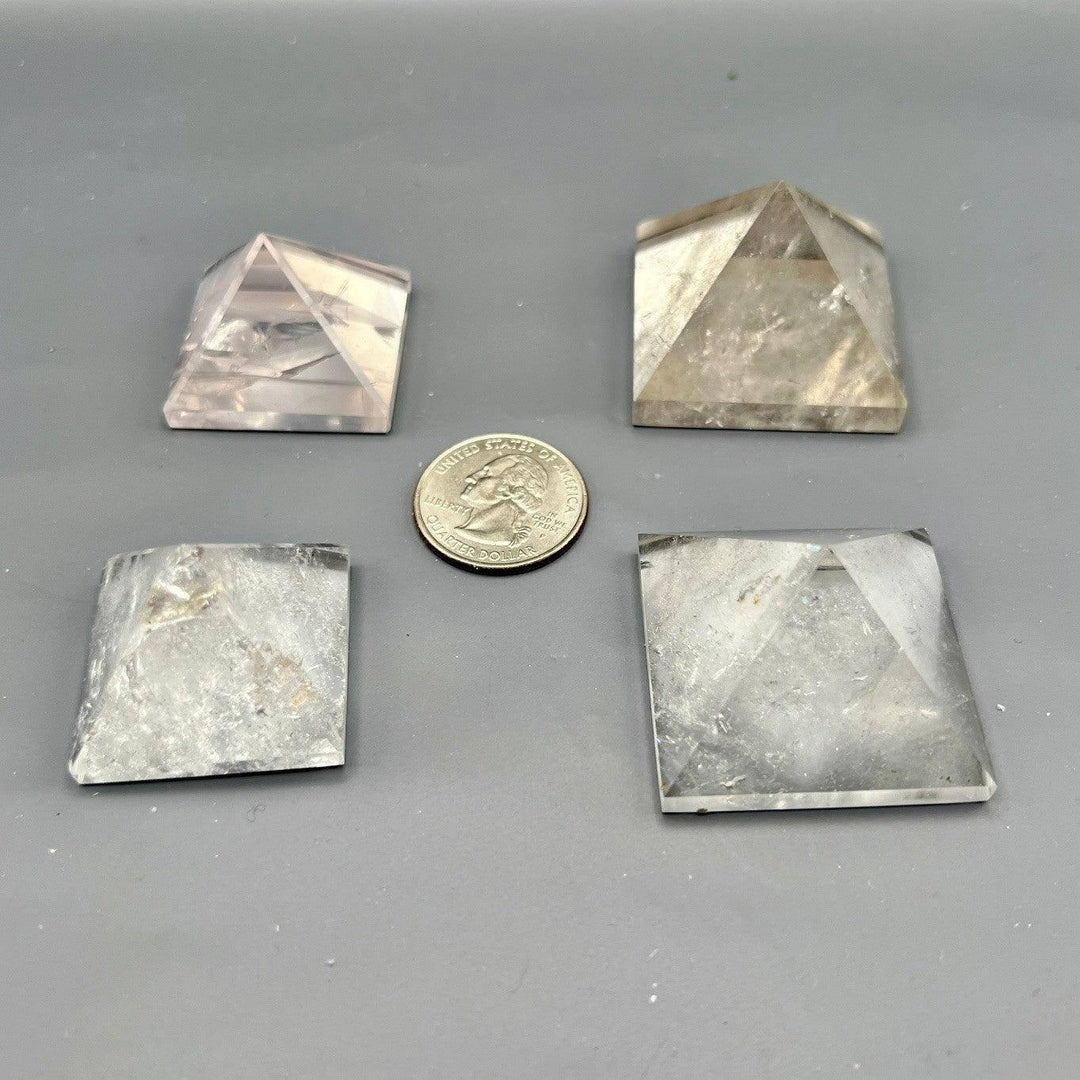 Four clear quartz crystal pyramids, varying in transparency and size, with a quarter for scale.