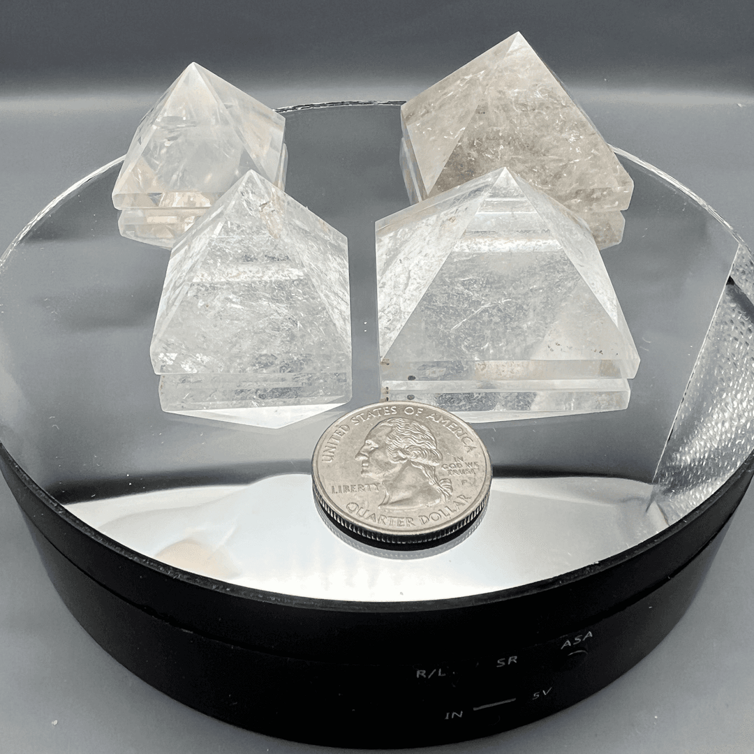 Four clear quartz crystal pyramids on a mirrored display, showcasing their clarity and light-enhancing properties.