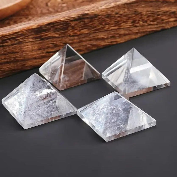 Four clear quartz crystal pyramids for chakra healing and meditation, on a dark surface.