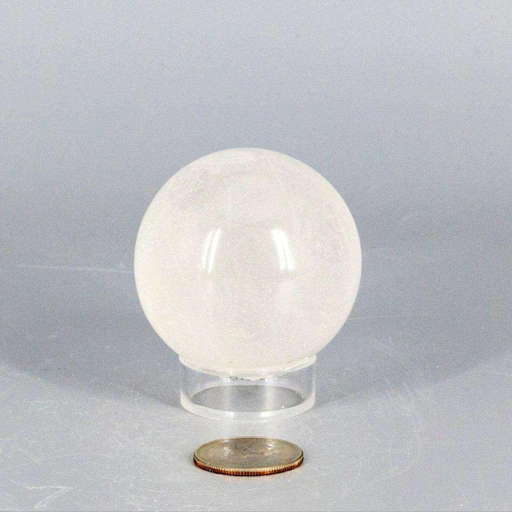Natural Quartz Sphere Master Healer, 53-55mm, clear polished crystal on a stand, with a coin for scale.