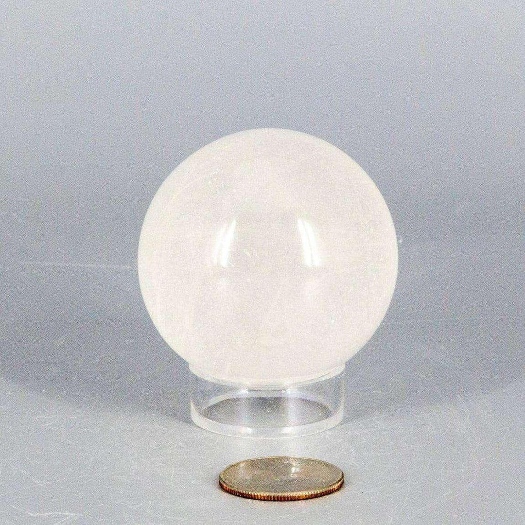 Natural Quartz Sphere Master Healer, 53-55mm, clear polished crystal on stand, with coin for scale.