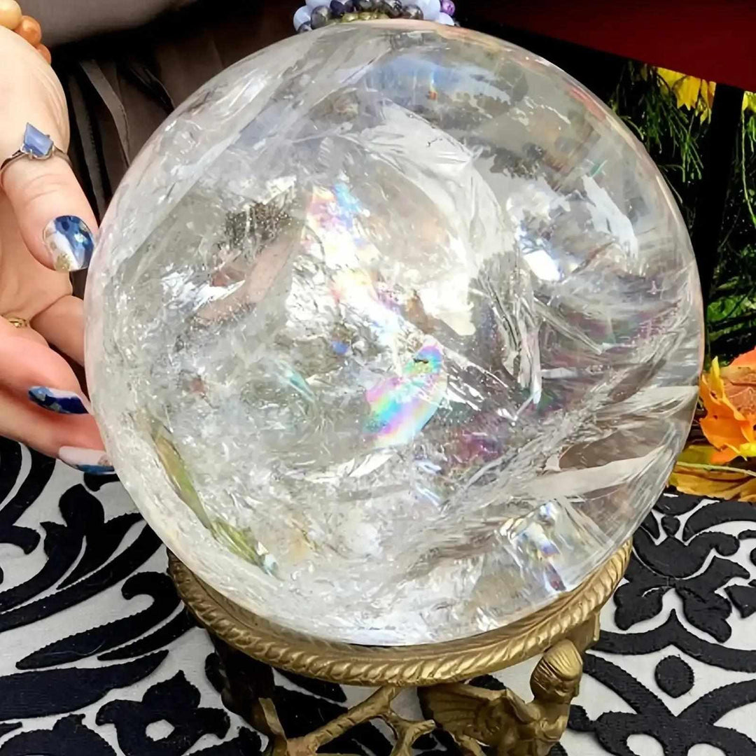 Polished Clear Quartz Crystal Sphere with internal veils, rainbow reflections, and Crown Chakra clarity on a gold stand.