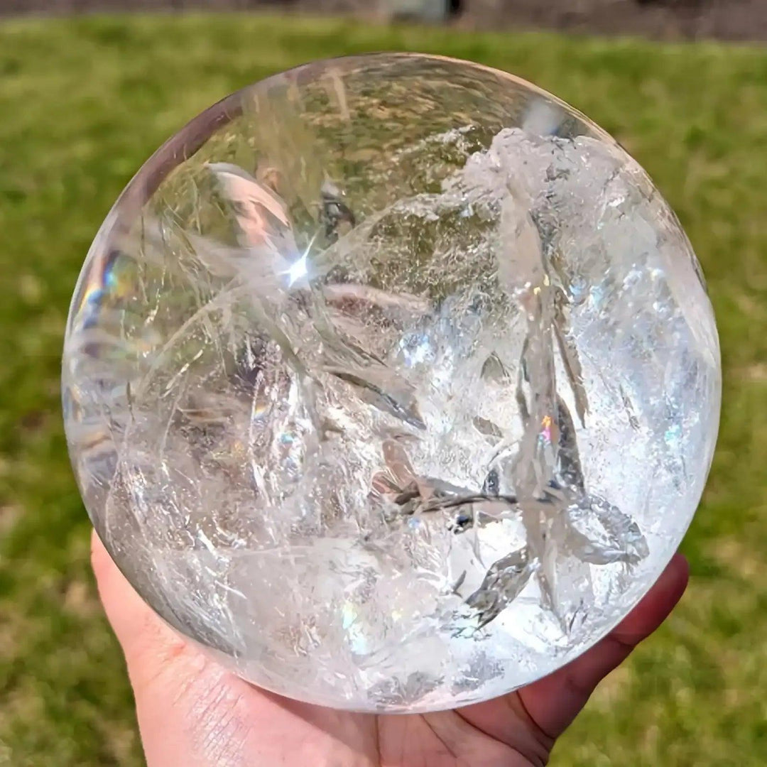 Polished Clear Quartz crystal sphere featuring internal veils and reflective light for Crown Chakra meditation focus.