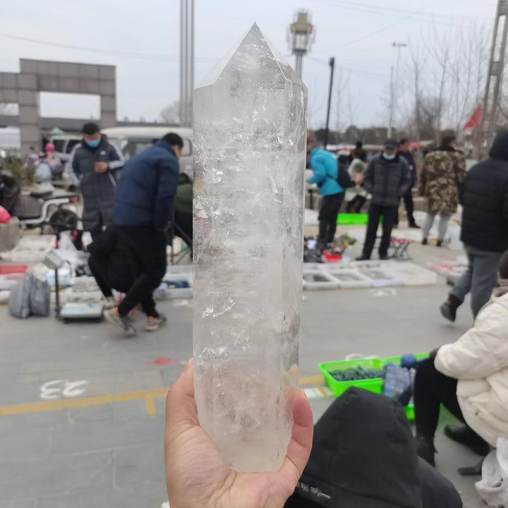 Substantial, clear quartz crystal tower obelisk, polished to a high finish, held in a hand.