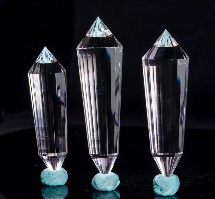 Three clear quartz crystal wands, 24-sided double points, standing on small turquoise bases.