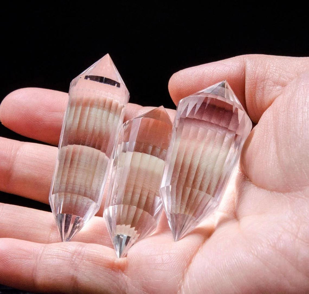 Three clear quartz crystal wands, 24-sided double point, held in a hand for spiritual healing.