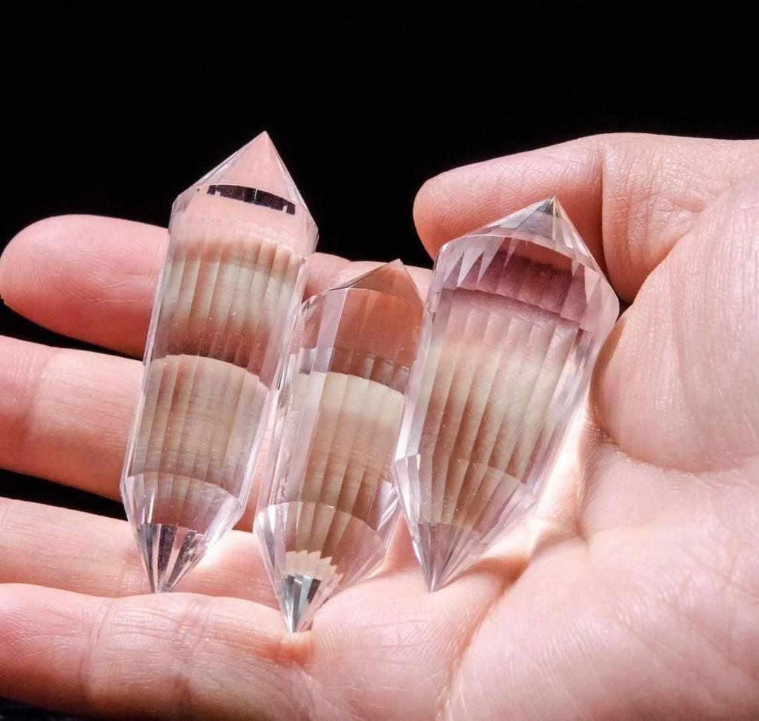 Three clear quartz 24-sided Vogel wands, double-pointed for amplified healing and focus, held in a hand.