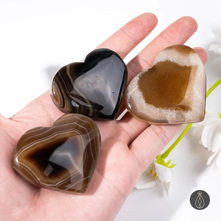 Hand holding three polished Coffee Agate crystal hearts in caramel, chocolate, and cream tones from Crystal Destiny.