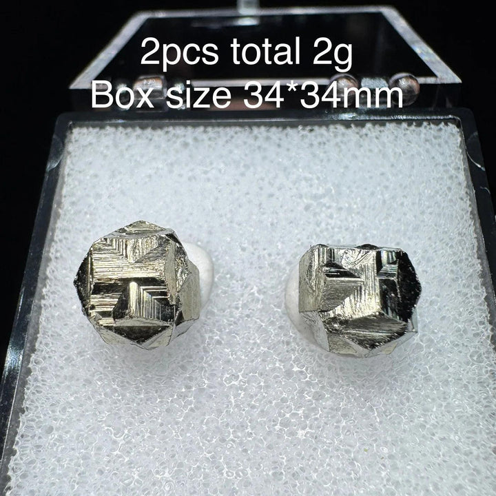 Two natural Colombia cross pyrite crystals in a 34x34mm display box, featuring metallic gold luster and unique geometric shapes.