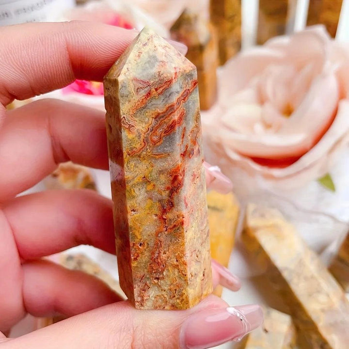Hand holding a Crazy Lace Agate crystal tower with swirling bands of cream, rust, gold, and pink.